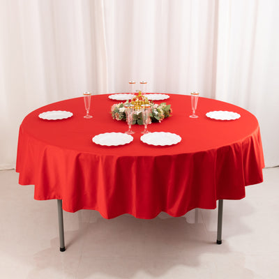 Round red tablecloth with white plates and decorative centerpiece.