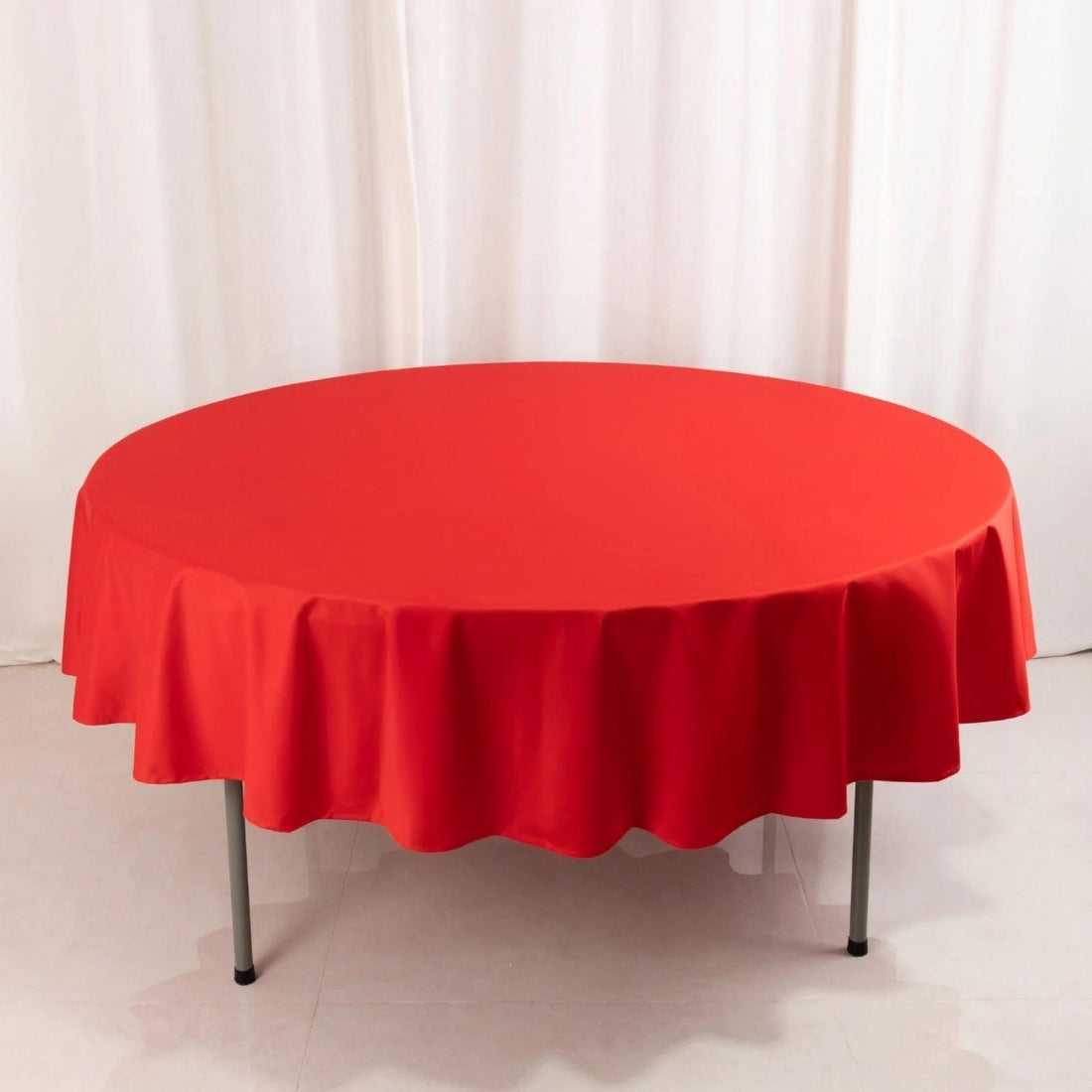 Red round tablecloth with scalloped edges on a plain backdrop.
