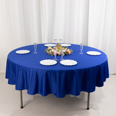 Round blue tablecloth draped over a table with white plates and floral centerpiece.