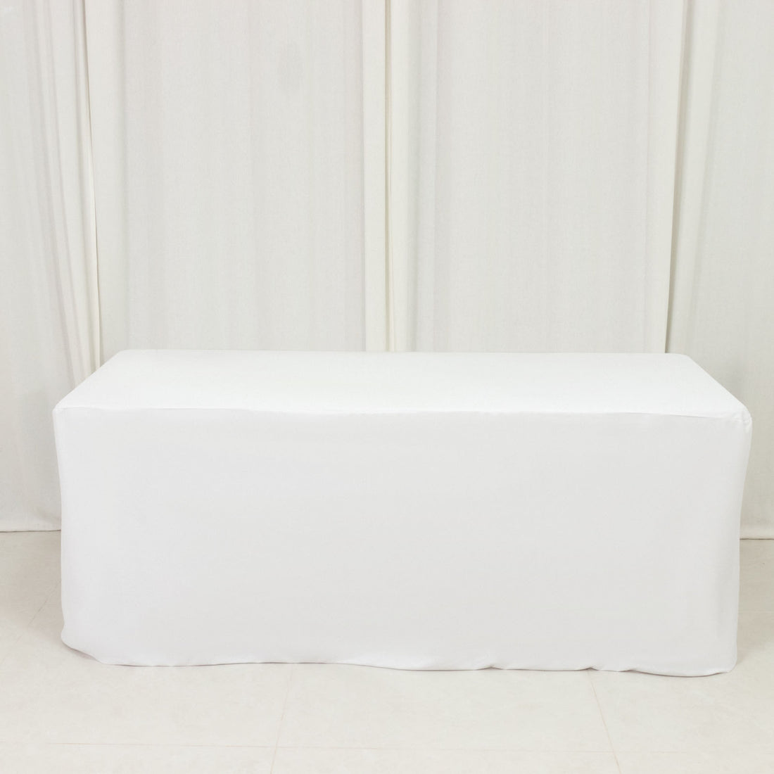 White table cover draped over a rectangular table in a studio setting.