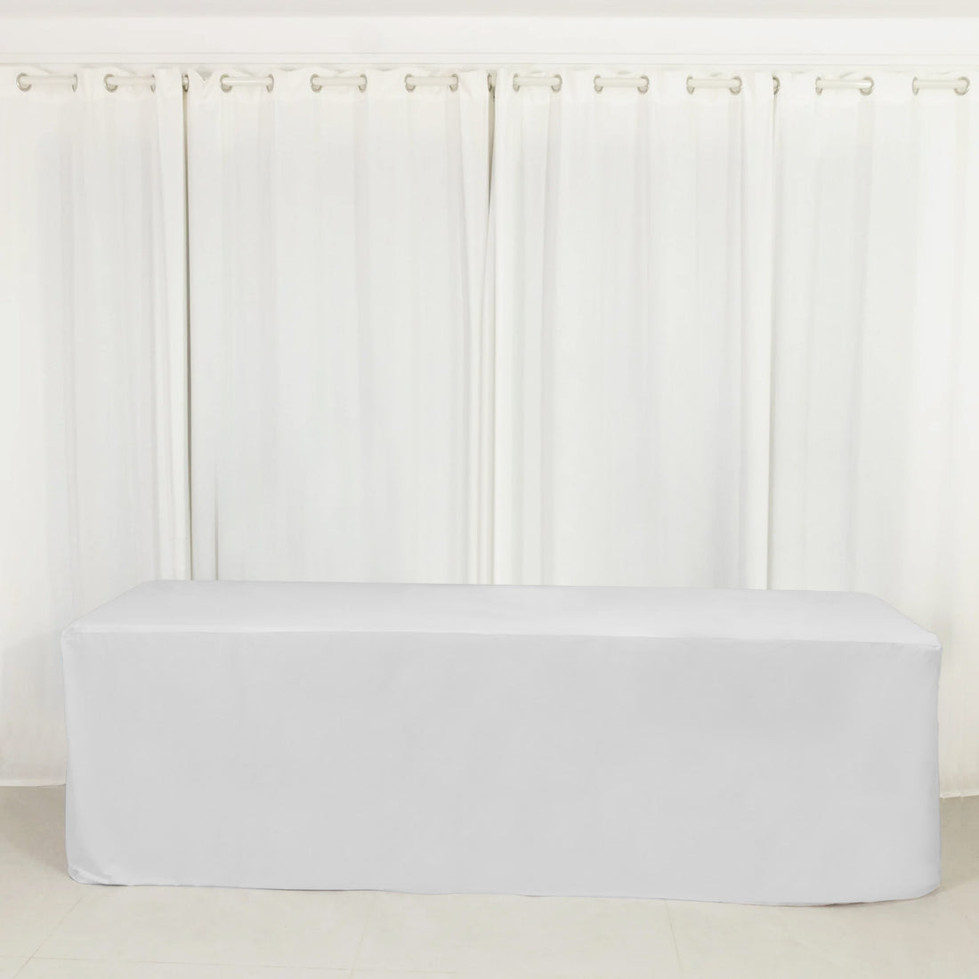 White table cover draped over a rectangular table in a bright room.