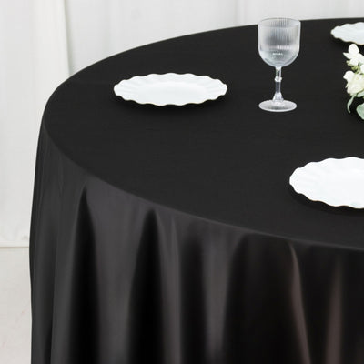 Black tablecloth draped over a round table with white plates and a glass.