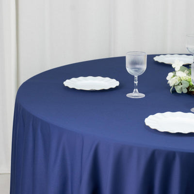 Navy round tablecloth with white plates and glassware on a table setting.