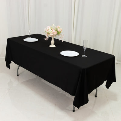 Elegant black tablecloth with plates and floral centerpiece for dining setup.