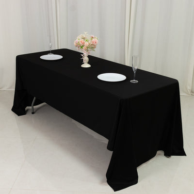 Black tablecloth draped over a table set with plates and a flower centerpiece.