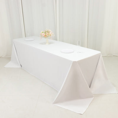 White table with a tablecloth, floral centerpiece, and glassware.