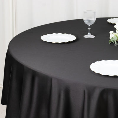 Black tablecloth draped over a round table with white plates and a glass.