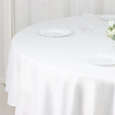 White round tablecloth on set dining table with plates and flowers
