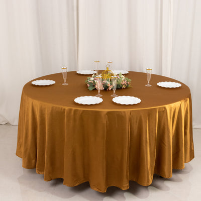 Round table with a gold tablecloth, plates, and floral centerpiece.