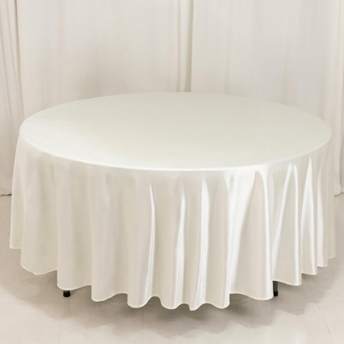 Round table covered with a white tablecloth in a studio setting.