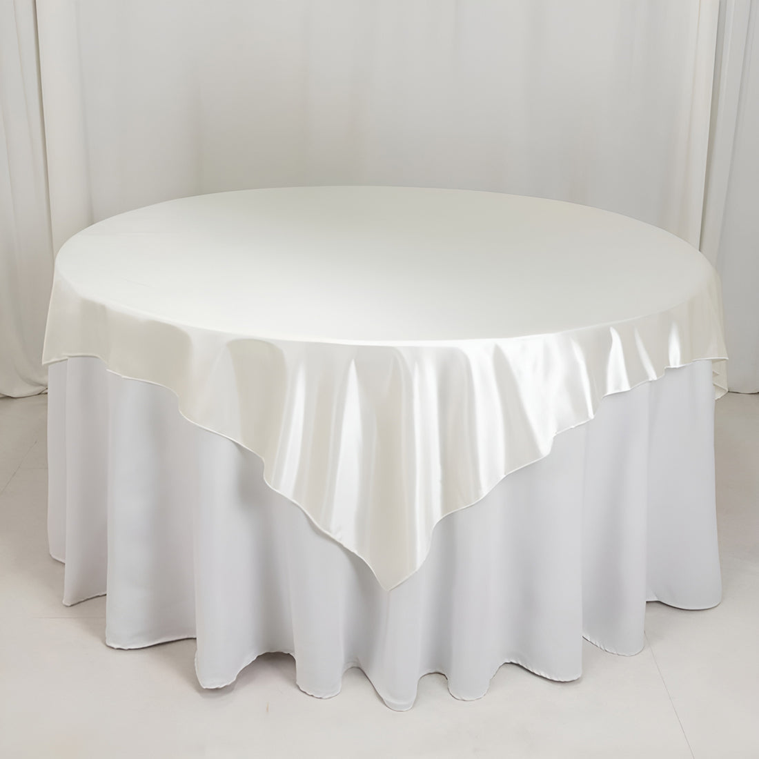 Round satin tablecloth in ivory, elegantly draped on a circular table.