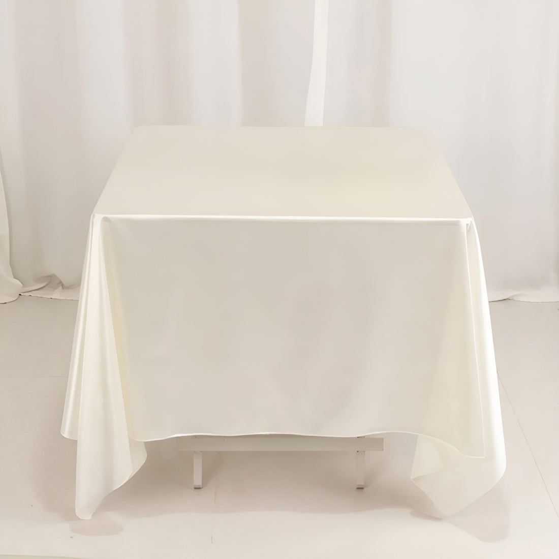 White satin tablecloth on a table against a plain backdrop