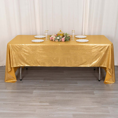 Gold sequin tablecloth on a dining table with floral centerpiece and plates.