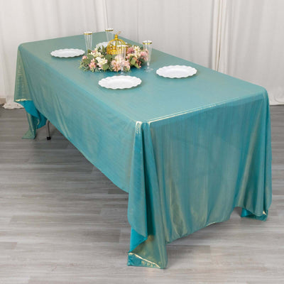 Teal tablecloth draped over a table with decorative plates and floral centerpiece.