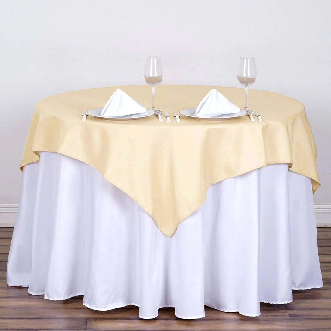 Elegant round table setting with yellow and white linens, glasses, and napkins.