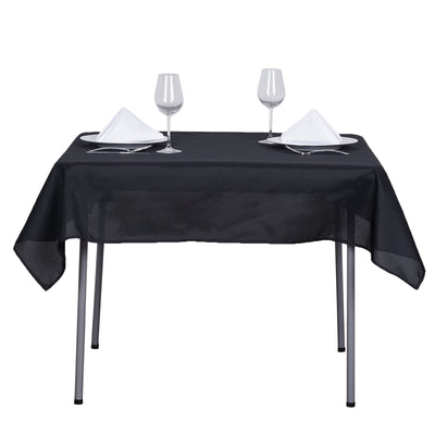 Black tablecloth on a dining table set for two with glasses and napkins.