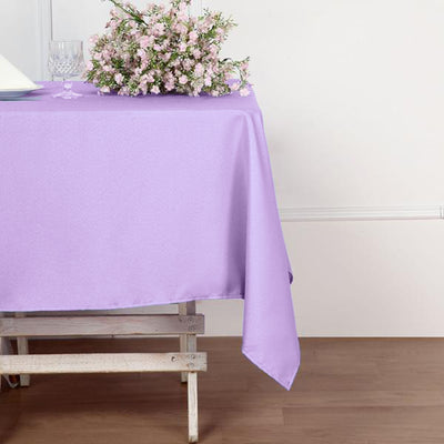 Purple tablecloth draped over a wooden table with flowers on top.