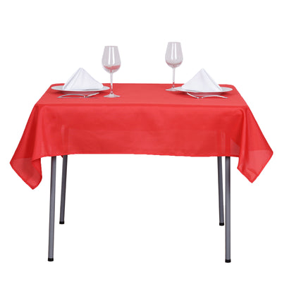 Red tablecloth set on a dining table with plates and glasses.