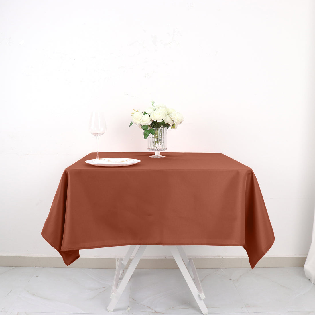 Brown tablecloth draped over a table with a glass and flowers.