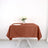 Brown tablecloth draped over a table with a glass and flowers.
