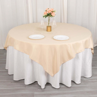 Round beige tablecloth draped over a table with plates and floral centerpiece.
