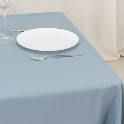 Blue tablecloth with a white plate, fork, and wine glass set on a dining table.