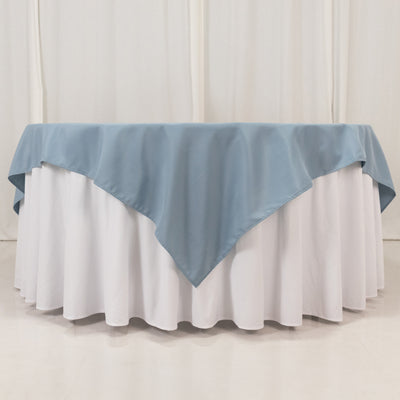 Blue tablecloth draped over a round table with white skirt.