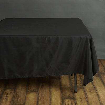 Black tablecloth draped over a table on a wooden floor.