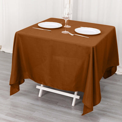 Brown tablecloth draped over a table set for two with plates and cutlery.