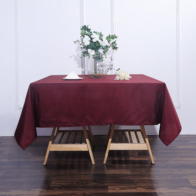Burgundy tablecloth draped over a wooden table with floral centerpiece.