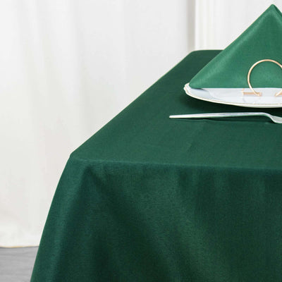 Green tablecloth with folded napkin and plate set on a table.
