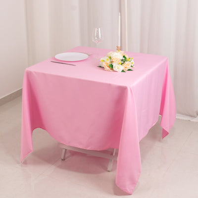 Pink tablecloth draped over a table set with a plate, glass, and flowers.