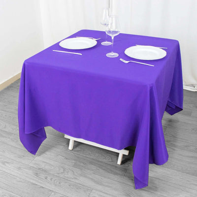 Purple tablecloth draped over a dining table set for two with plates and glasses.