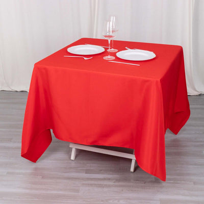 Red tablecloth set with plates and glasses on a square table.
