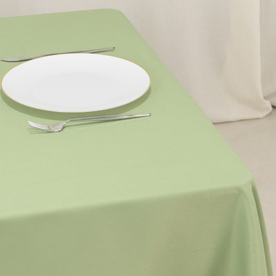 Green tablecloth with a white plate and silver utensils on a simple setting.