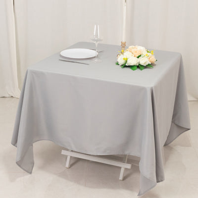 Gray tablecloth draped over a table set for dining with flowers and glassware.