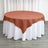 Round table with a rust-colored tablecloth on a white table skirt.