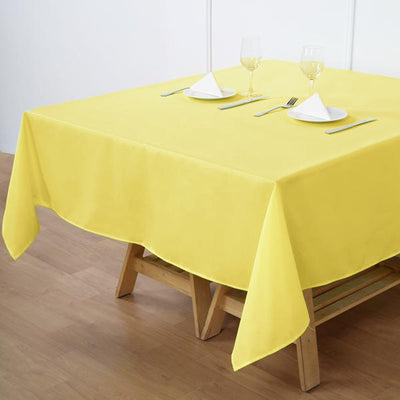 Yellow tablecloth on a wooden table set with glasses and napkins.