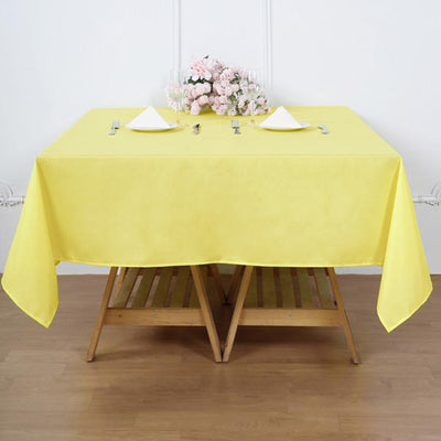 Yellow tablecloth draped over a wooden table set for dining with flowers.