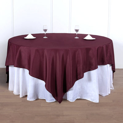 Round burgundy tablecloth draped over a white table with glasses and napkins.
