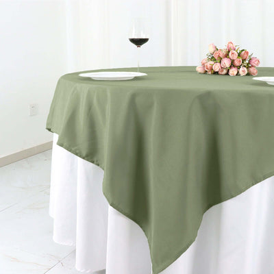 Olive green tablecloth on a round table with wine glass and flowers.