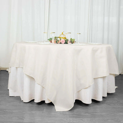 Elegant round table covered with a cream tablecloth and floral centerpiece.