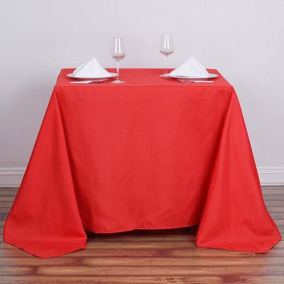 Red tablecloth draped over a table set for dining with glasses and plates.