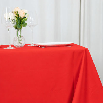 Red tablecloth with wine glasses, roses, and white dinner plate at a dining table