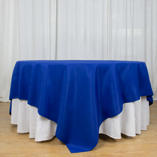 Blue tablecloth over a round table with white drape backdrop