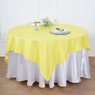 Yellow round tablecloth draped over a silver table cover in a dining setup.