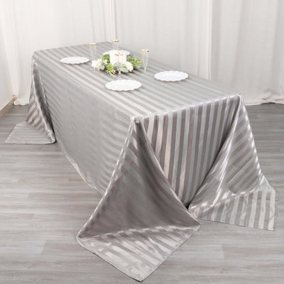 Silver striped tablecloth on a dining table with plates and floral centerpiece.