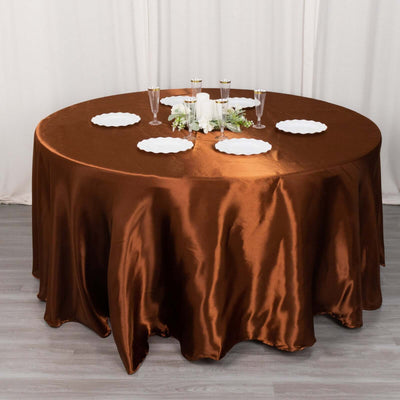 Round bronze satin tablecloth on a set dining table with plates and glasses.