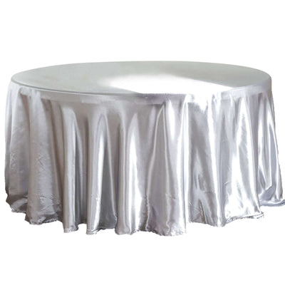 Round silver tablecloth with elegant draping on a plain backdrop.