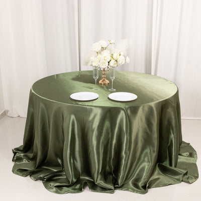 Elegant olive green tablecloth draping over a round table with plates and flowers.
